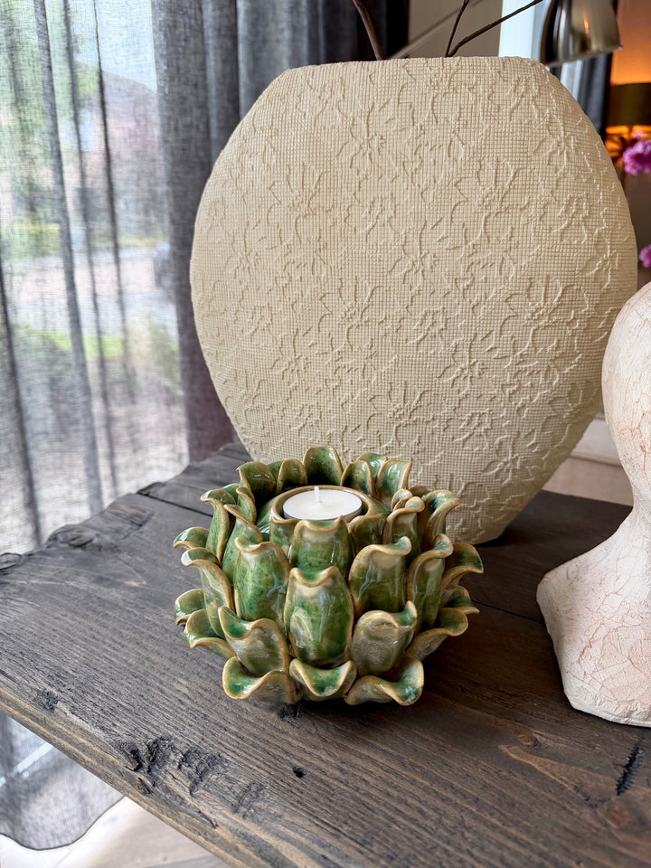 Crèmekleurige vaas met organische structuur en groene keramieken kandelaar op houten sidetable