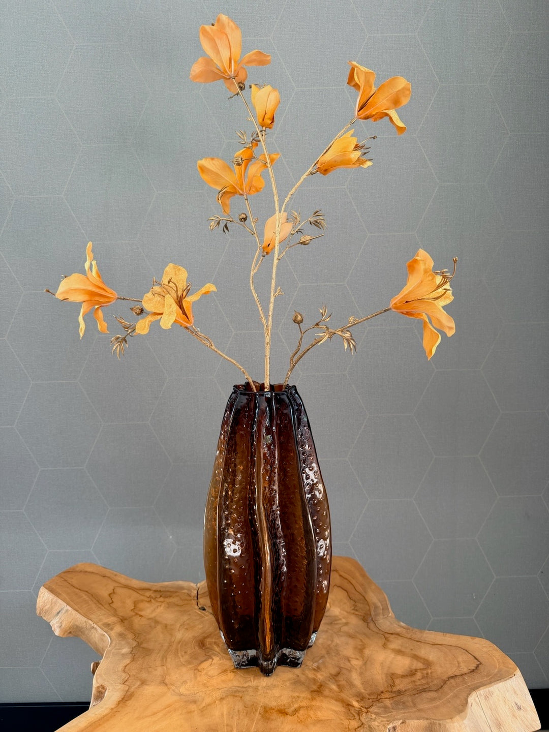 Hoge amberkleurige glazen vaas met oranje zijden bloemen op houten tafel