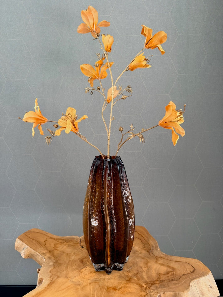 Hoge amberkleurige glazen vaas met oranje zijden bloemen op houten tafel
