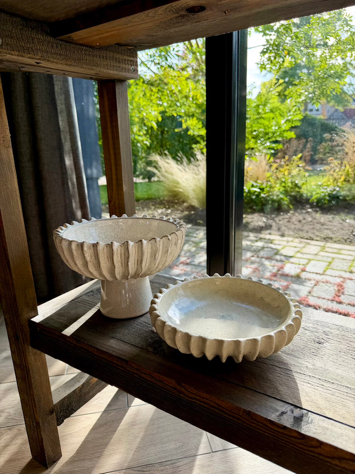 Beige keramieken schaal van 20 cm naast een bijpassende schaal op voet, ter inspiratie
